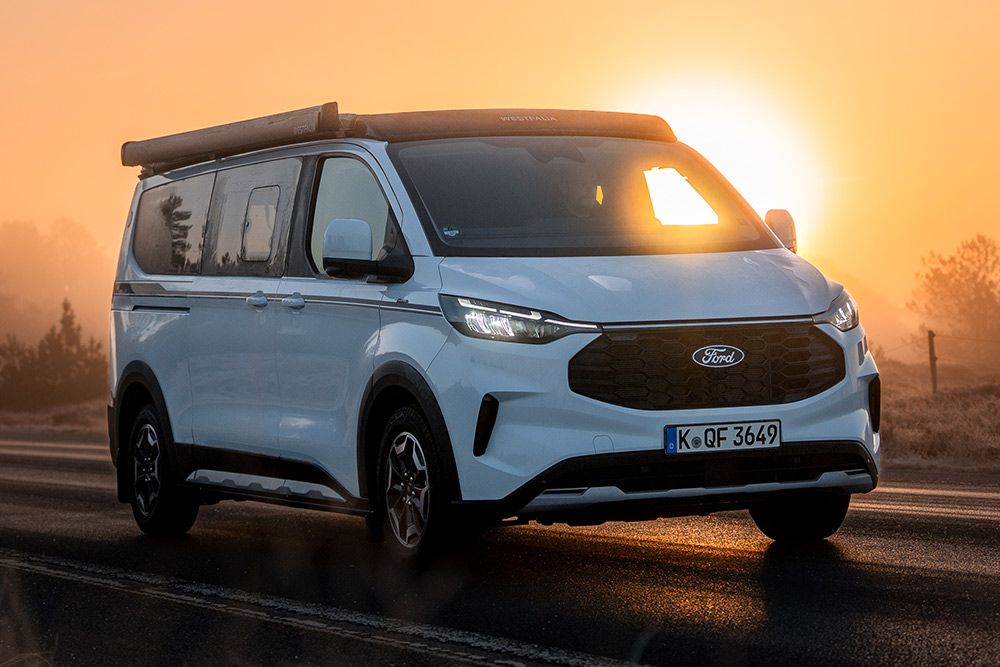 Frontansicht der Ford Nugget Jubiläumsedition auf einer asphaltierten Straße in einer nebligen Landschaft bei Sonnenaufgang.