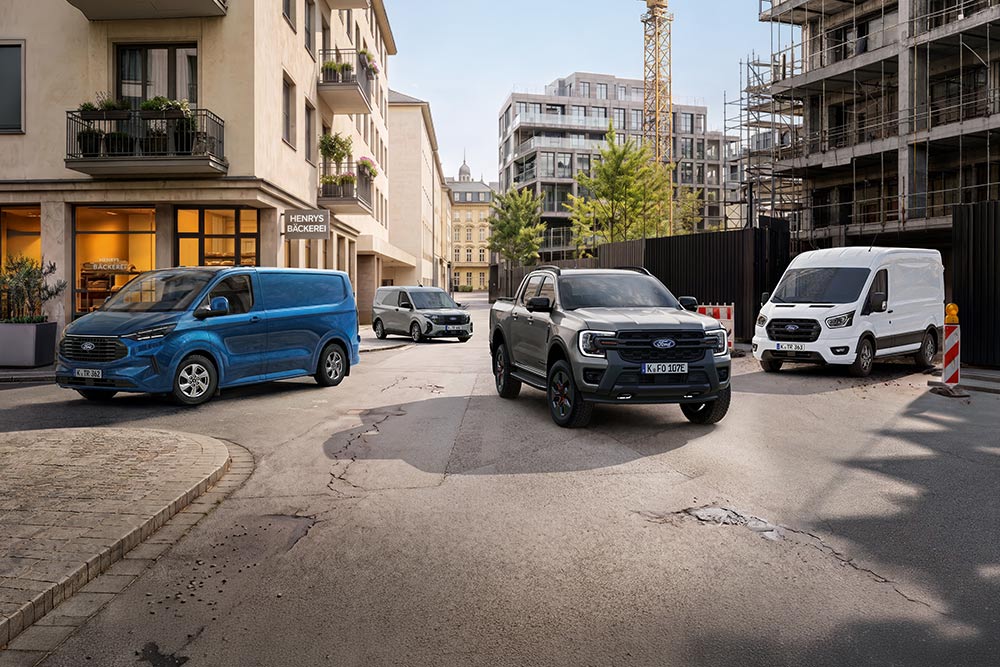 Vier Ford Nutzfahrzeuge, darunter ein grauer Ranger Pickup und blaue sowie weiße Transit Transporter, stehen auf einer Stadtstraße. 