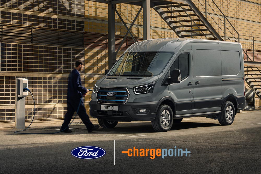 Person lädt einen grauen Ford E-Transit Transporter an einer Ladestation im Freien auf.