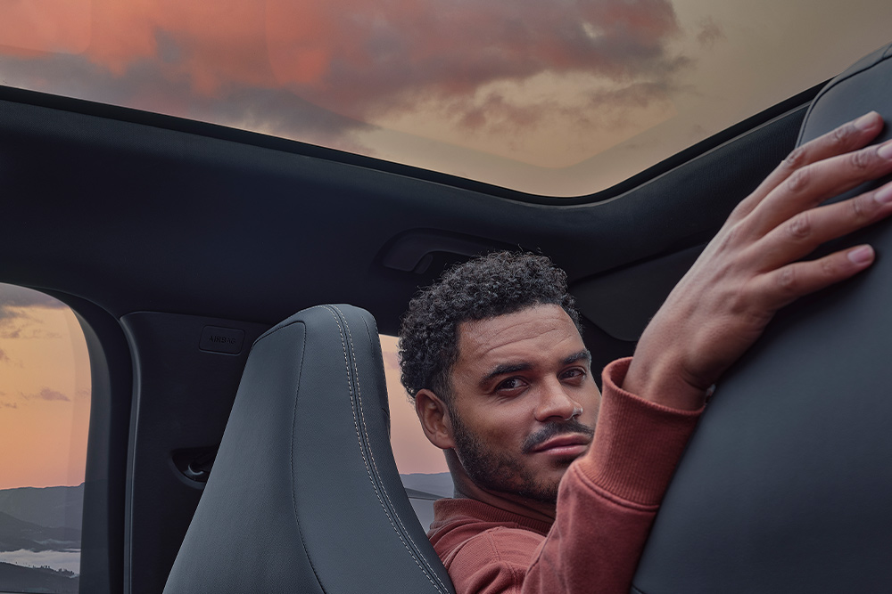 Eine Person sitzt bei Sonnenuntergang in einem Auto, die Hand auf der Rückenlehne eines Sitzes.