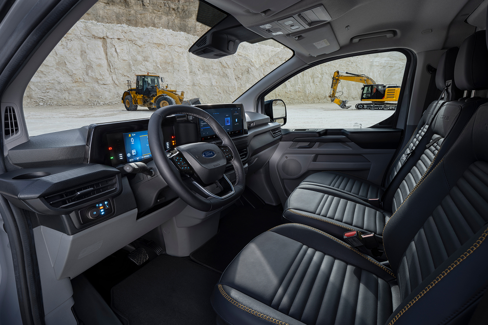 Der Innenraum eines Ford E-Transit Custom Elektro-Vans mit Sitzen und Lenkrad, geparkt in einem Steinbruch. 