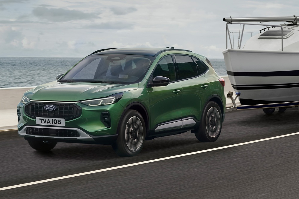 Ein grüner Ford Kuga, der ein kleines Boot entlang einer Küstenstraße zieht.