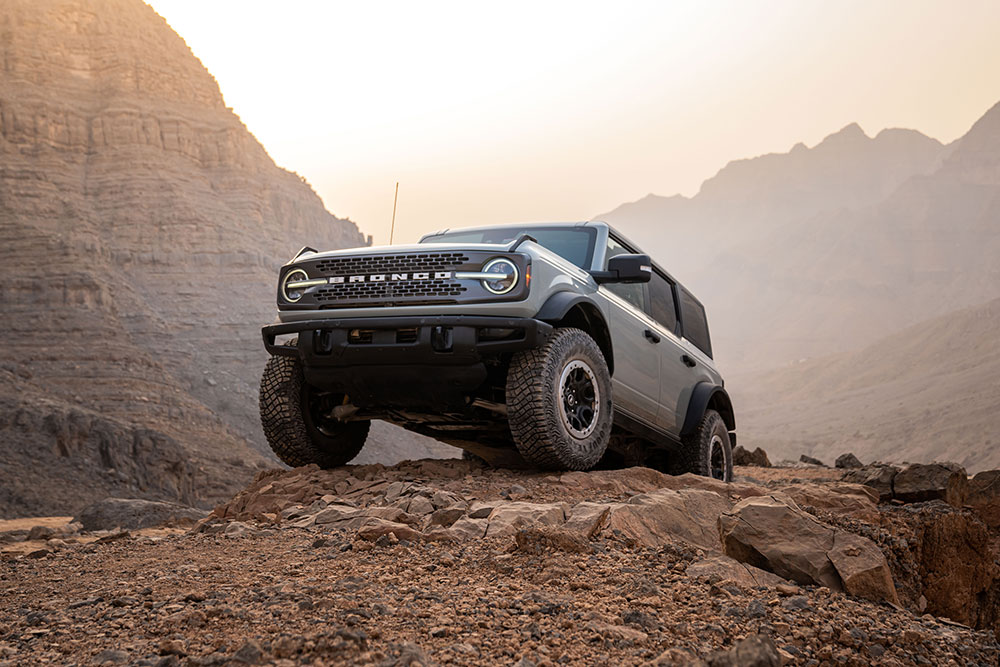 Ein grauer Ford Bronco parkte auf einem felsigen Pfad in einer Bergkulisse.