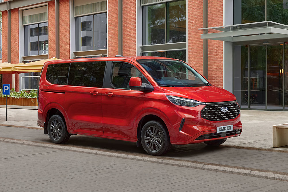 Roter Ford Tourneo Custom parkt auf einer Stadtstrasse vor einem Backsteingebaeude.