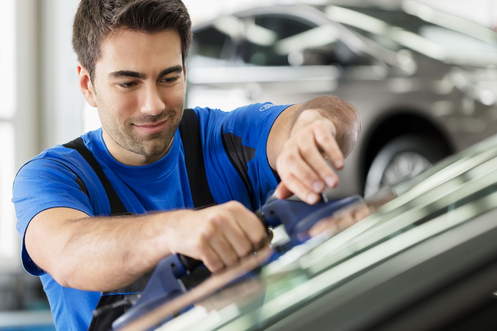 Durch die Scheibe sind eine Person zu sehen, die im Wartebereich einer Ford-Werkstatt telefoniert, ein Transporter auf einer Hebebühne und ein blauer Pkw.
