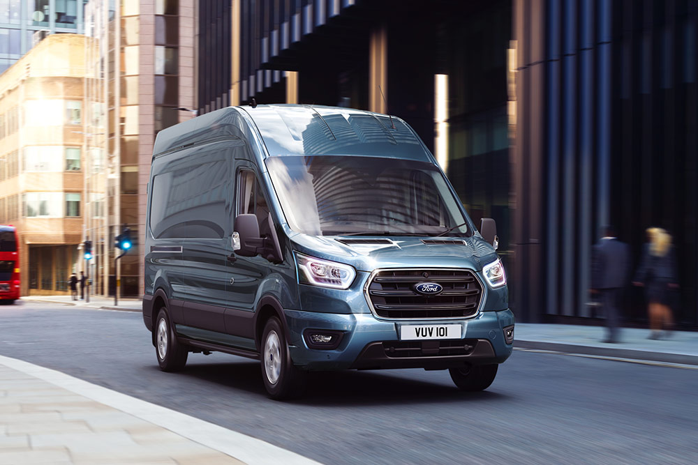 Ein blau-grauer Ford Transit  fährt auf einer Straße.