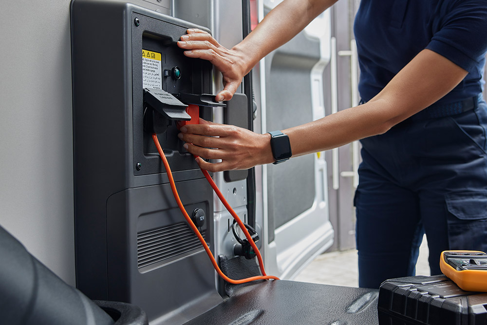 Nahaufnahme einer Person, die ein Ladekabel in einem Ford E-Transit Kastenwagen einsteckt.