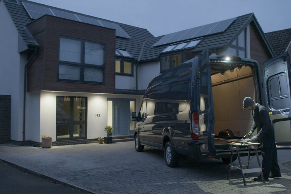 Ein Zimmermann arbeitet nachts hinter einem Ford Transit mit geöffneten Hecktüren, beleuchtet durch die LED-Außenleuchte.