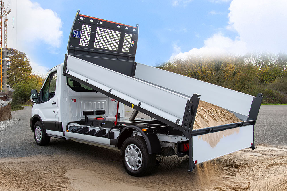 Weißes Ford Pro Fahrgestell mit erhöhtem Pritschenaufbau parkt auf einer Baustelle.