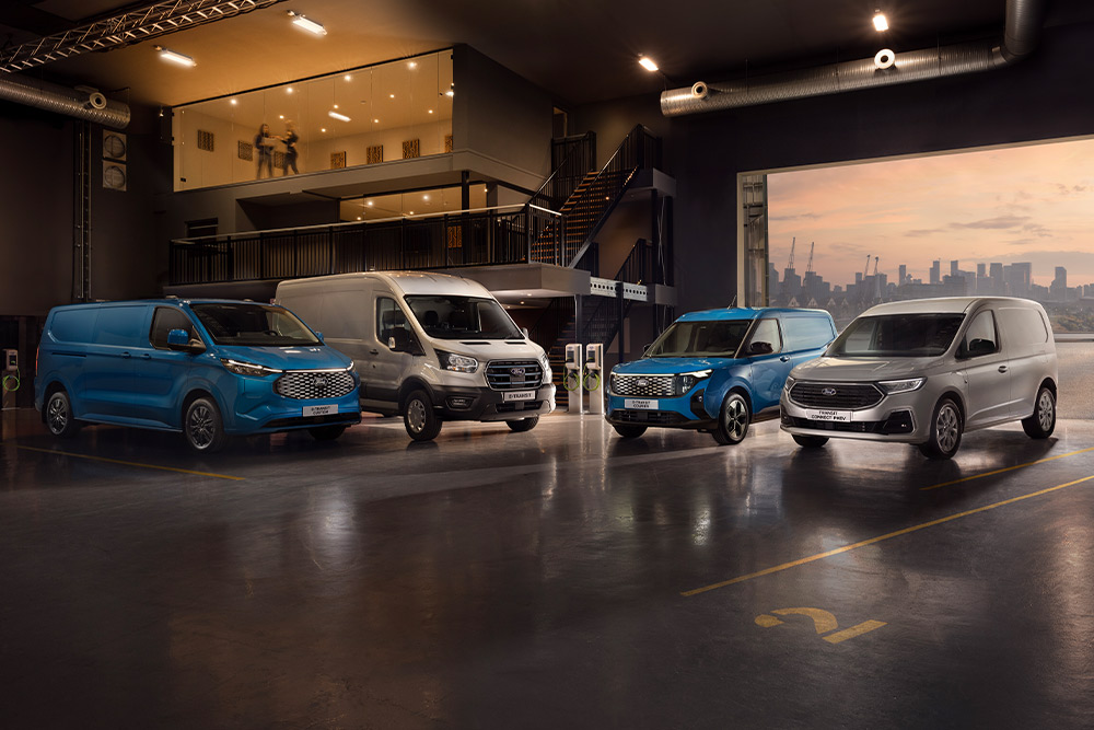 Flotte von Ford Transits in einem Ausstellungsraum mit einer Stadtkulisse bei Dämmerung im Hintergrund.