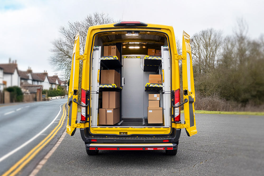 Rückansicht eines gelben Ford Transit Transporters mit offenen Türen, der einen organisierten Innenraum mit Regalen und Kisten zeigt.