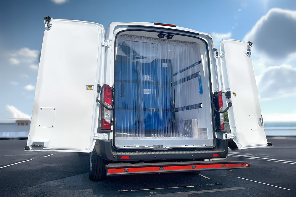 Rückansicht eines weißen Ford Transit Kühltransporters mit offenen Türen und Kunststoffstreifenvorhängen.
