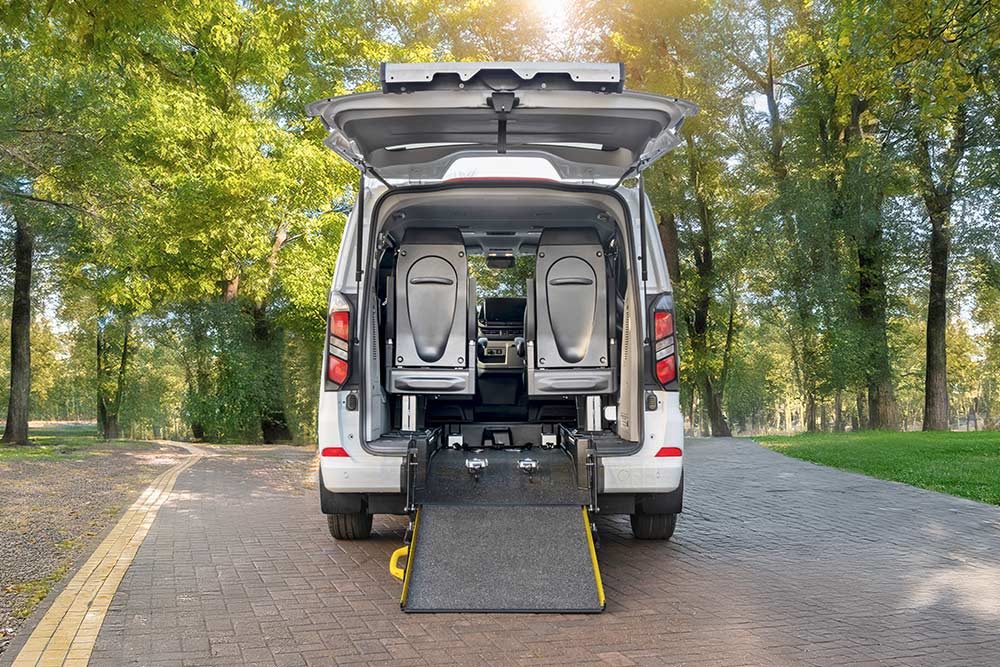 Rückansicht eines weißen Ford Transit Custom mit offener Heckklappe und ausgefahrener Rollstuhlrampe.