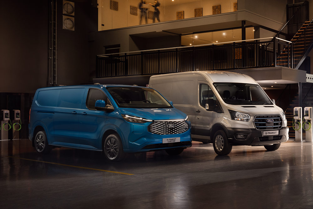 Ein blauer Ford E-Transit Custom und ein silberner Ford E-Transit laden auf einem Parkplatz.