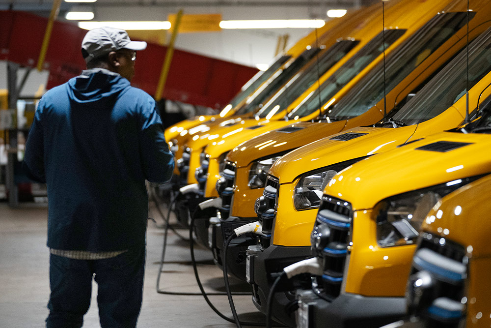 Eine Reihe gelber elektrischer Ford-Transporter wird geladen, ein Mann steht daneben.