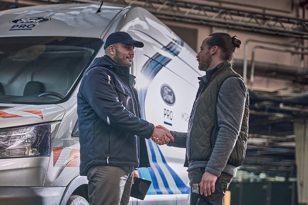 Ford Pro Techniker spricht mit Kunde, ein Ford Pro Mobile Service Transporter ist im Hintergrund sichtbar.