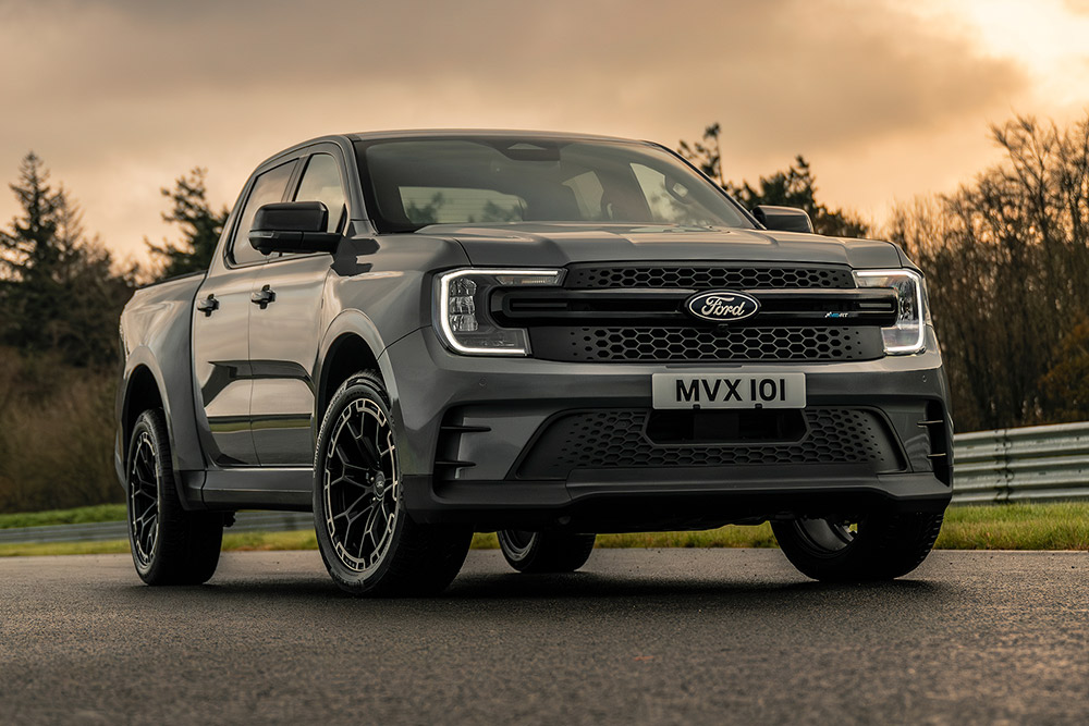 Grauer Ford Pro Ranger Plug-in Hybrid parkt auf einer nassen Straße, Bäume im Hintergrund.