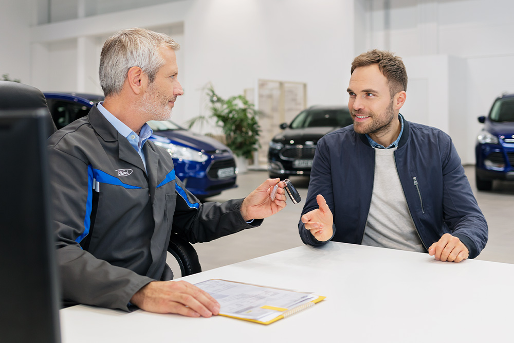 Zwei Männer sitzen sich in einem Ford-Autohaus gegenüber.