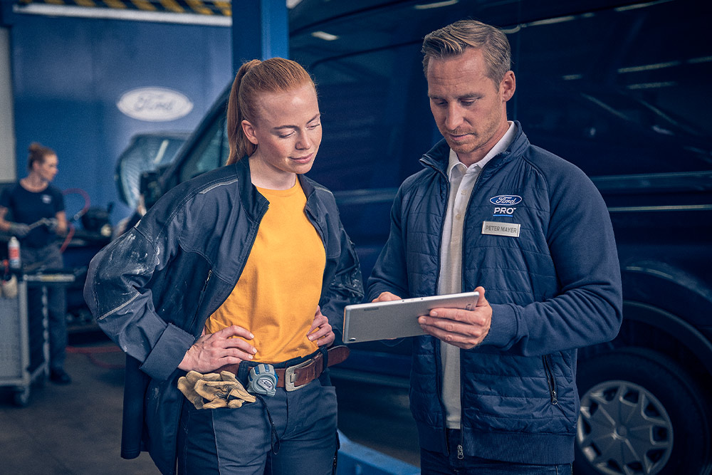 Ford-Techniker und Flottenmanager überprüfen Daten auf einem Tablet in einer Werkstatt.