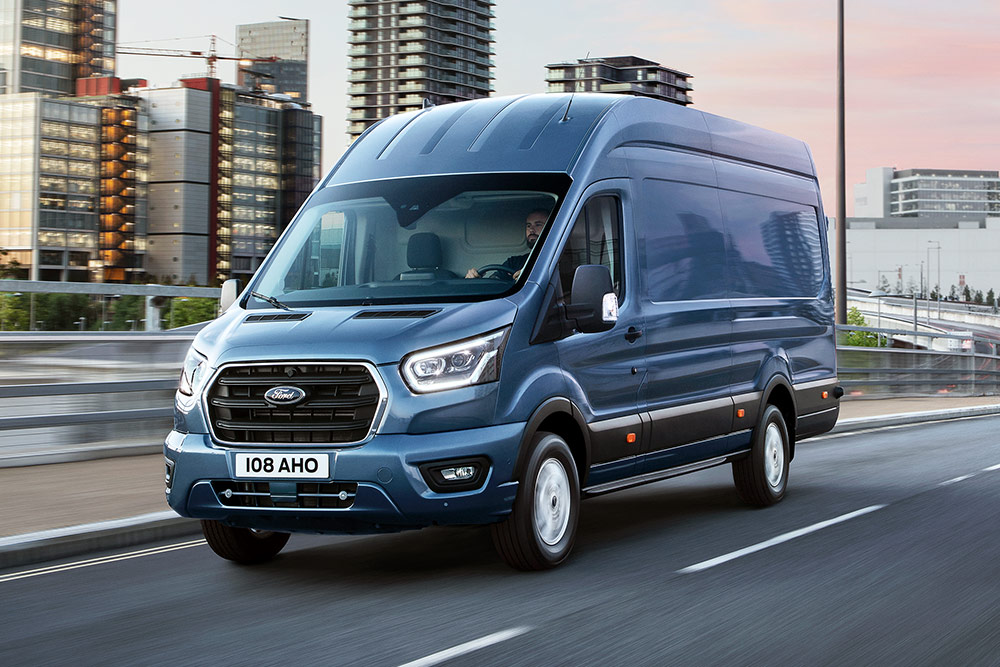 Ein Ford Transit fährt über eine Brücke, im Hintergrund eine bebaute Stadtlandschaft.