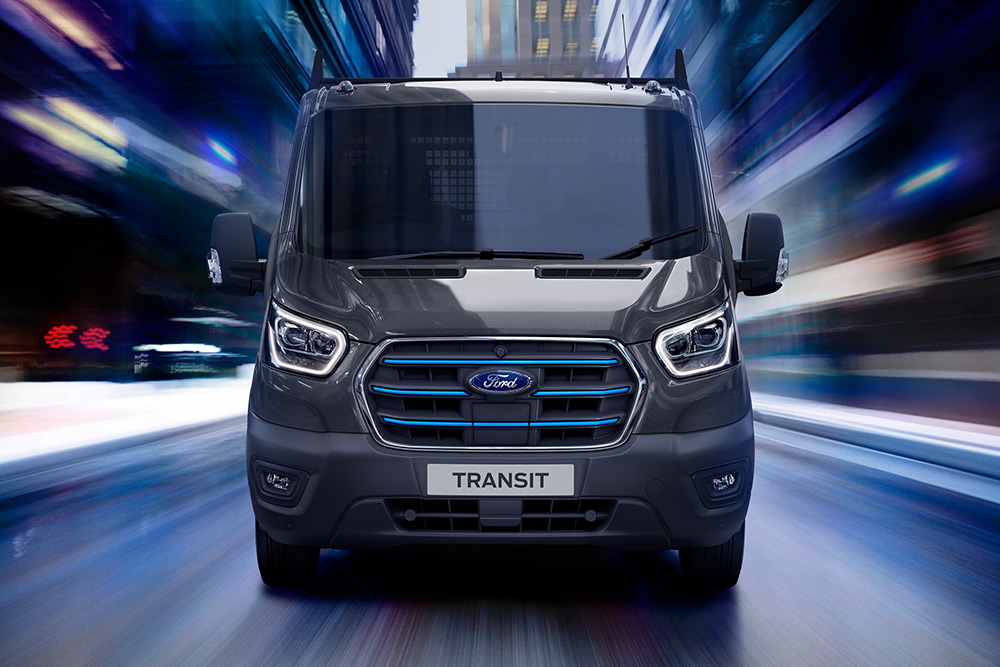 Silberner Ford Pro Transit auf einer Baustelle geparkt, Bauarbeiter im Hintergrund.