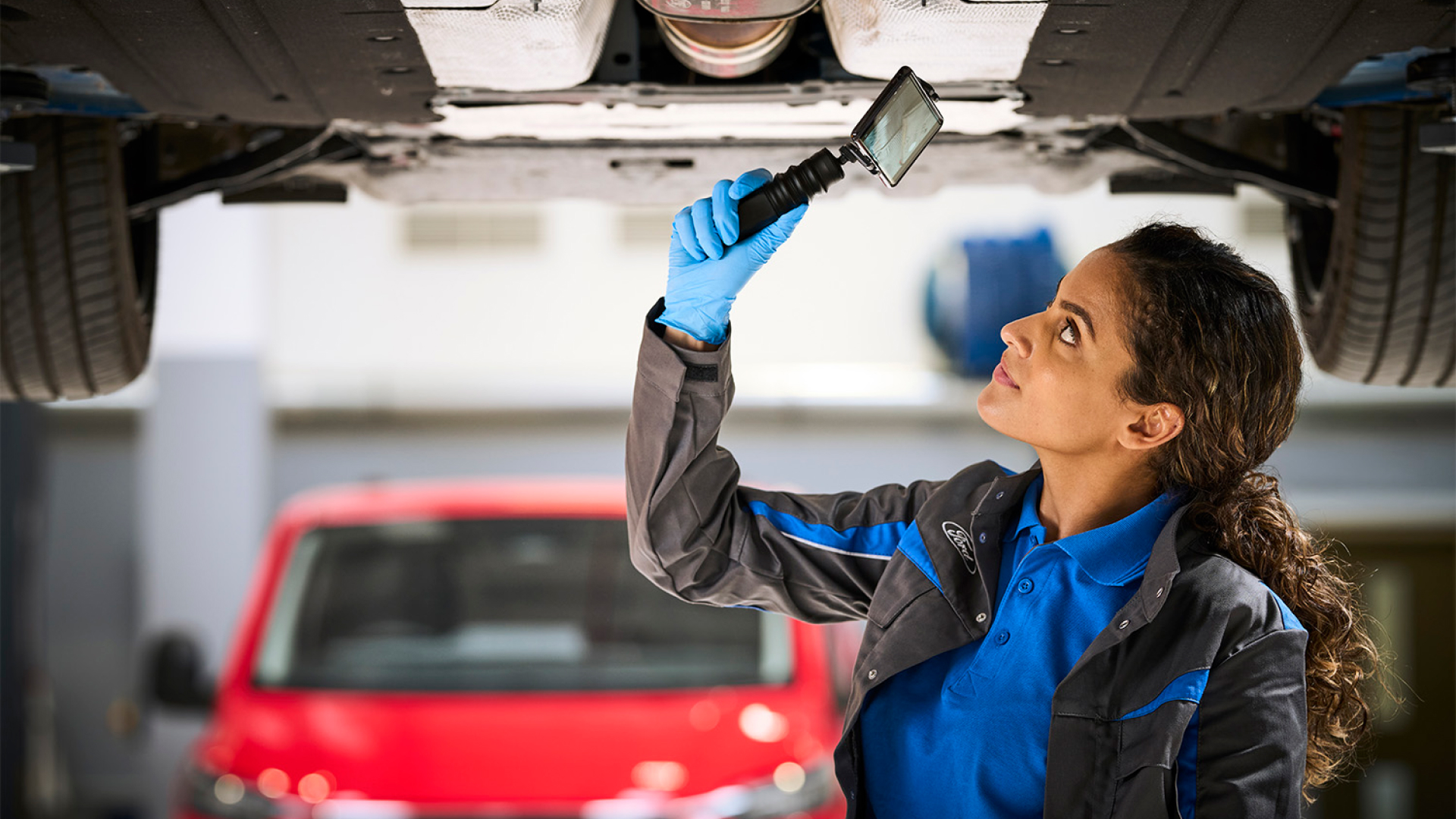 Mechaniker inspiziert die Unterseite eines Autos mit einem Handspiegel.