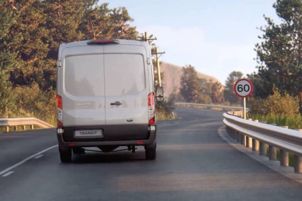 Ford Transit in Silber in der Heckansicht auf Landstraße mit Verkehrsschild fahrend